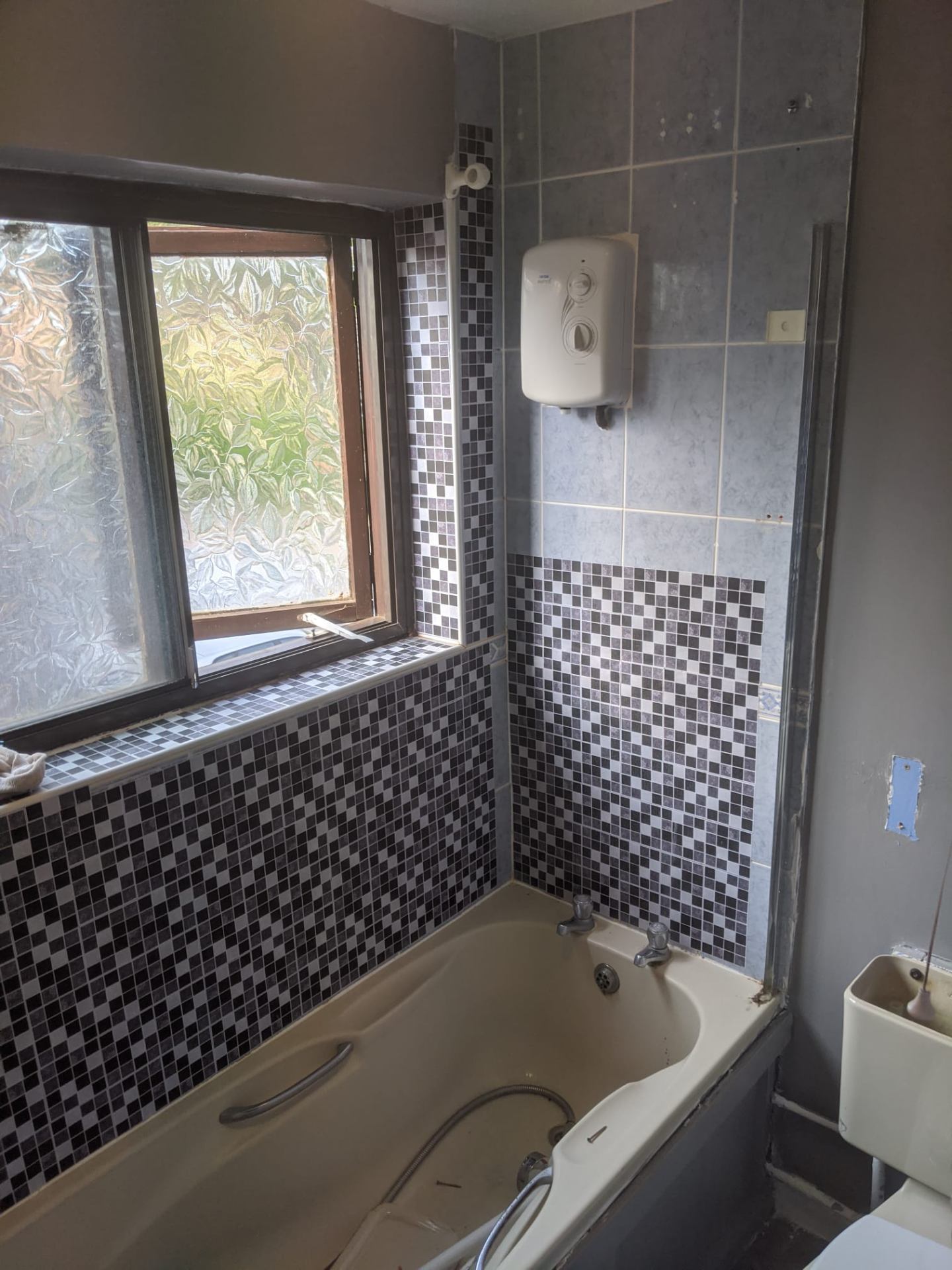 Old blue-tiled bathroom with bath and electric shower