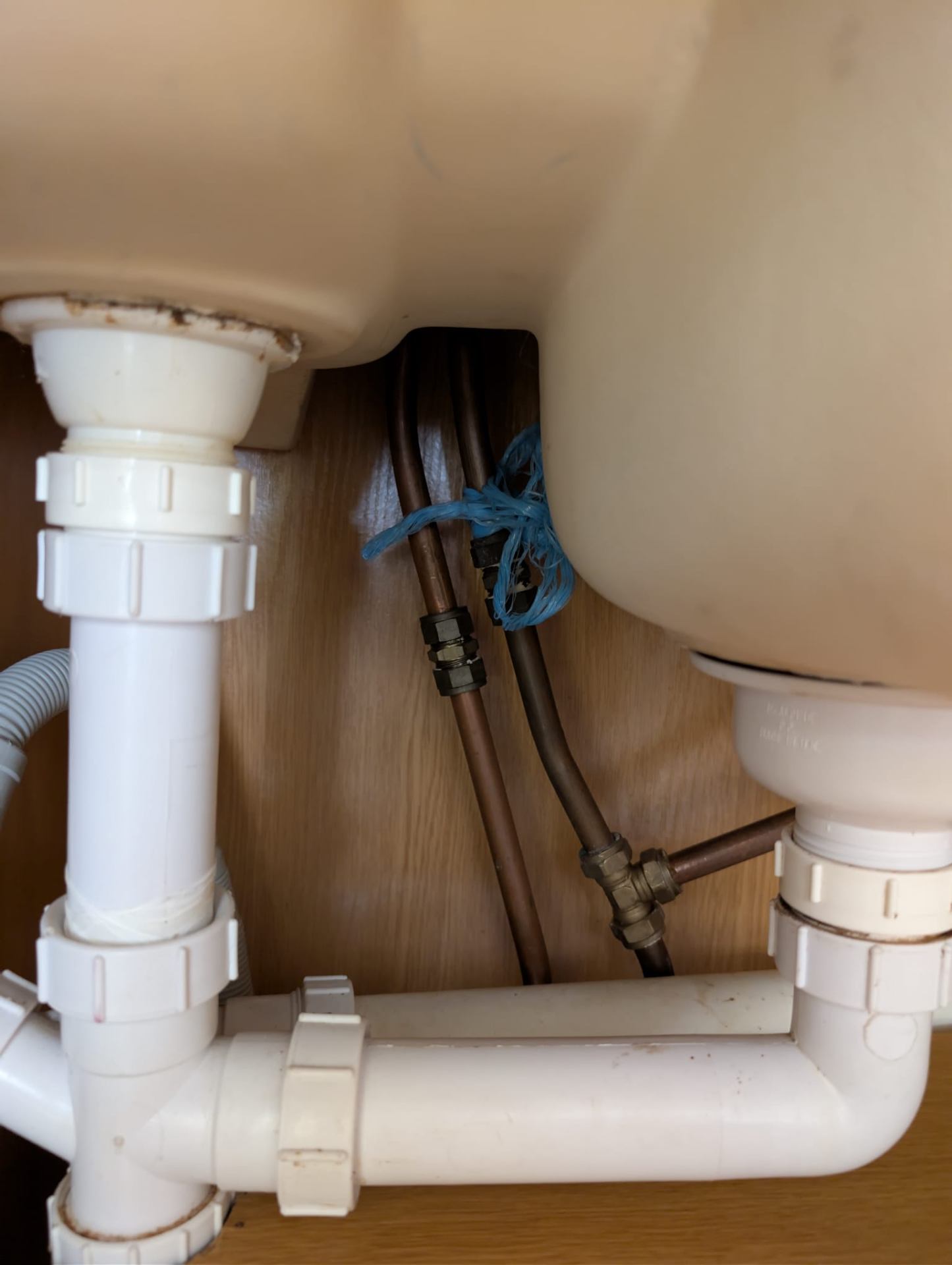 Untidy copper pipework and plastic traps beneath a sink