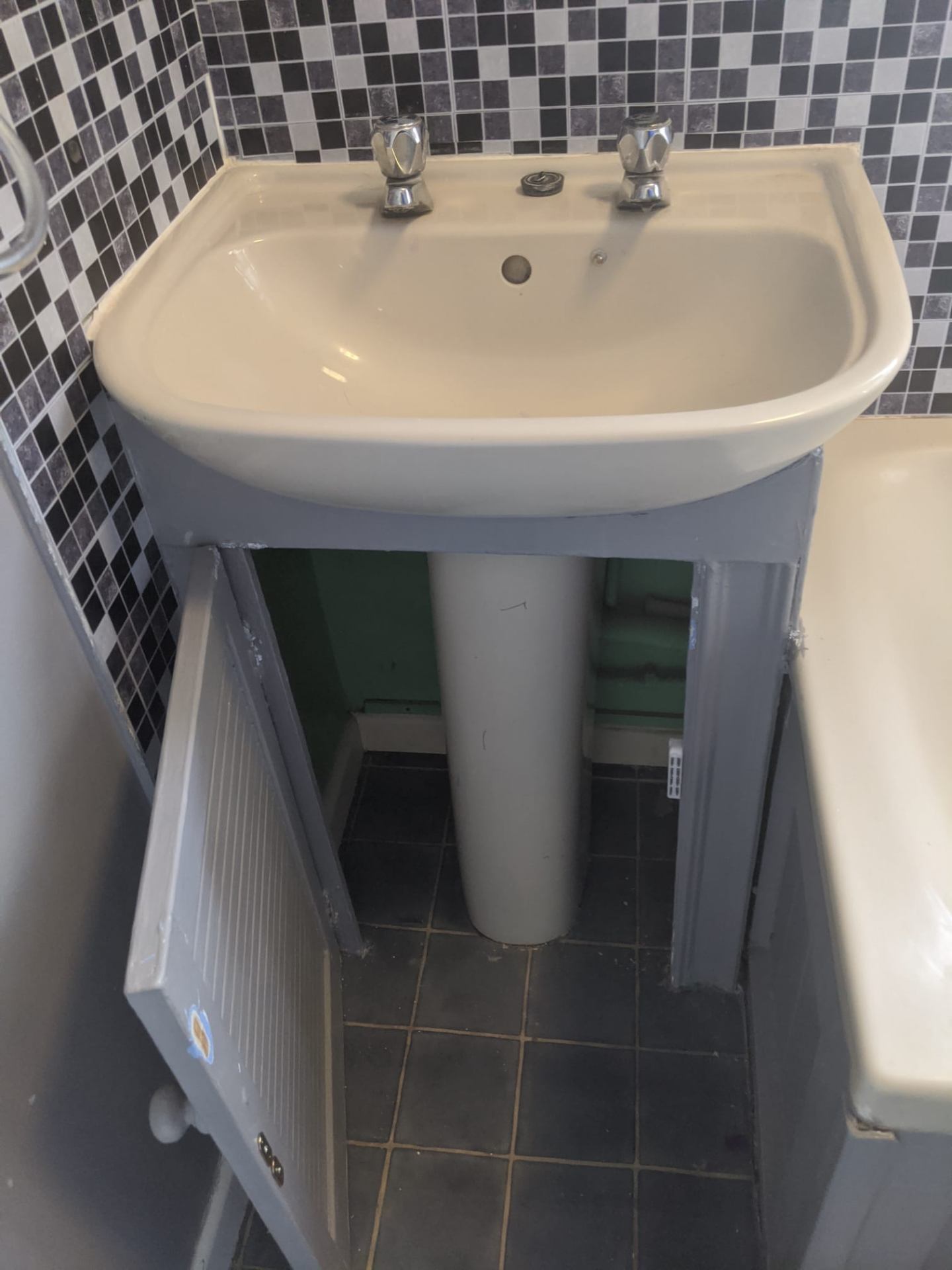 Dated bathroom sink with exposed pipework and old tiling