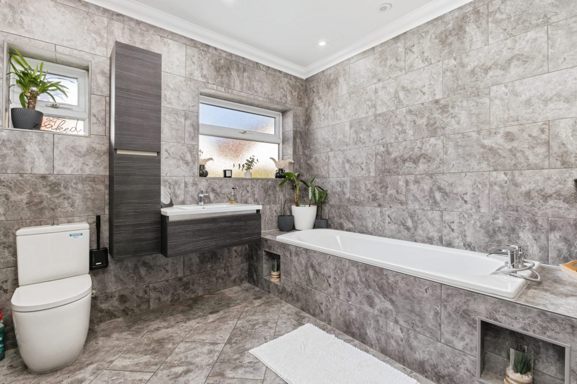 Completed bathroom with large grey marble-effect tiles, floating vanity unit and freestanding bath