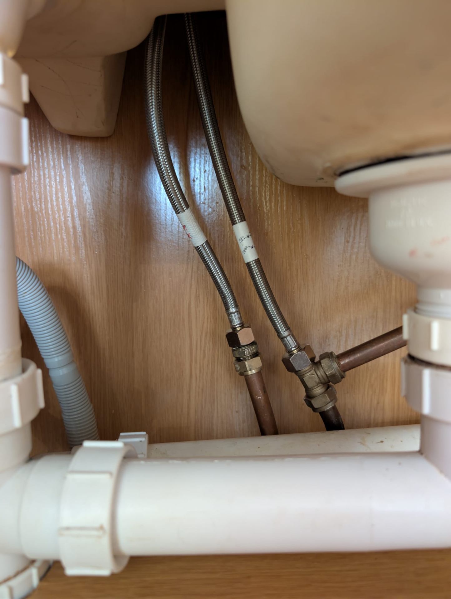 Neat, reorganised waste pipework and flexible supply connections under a sink